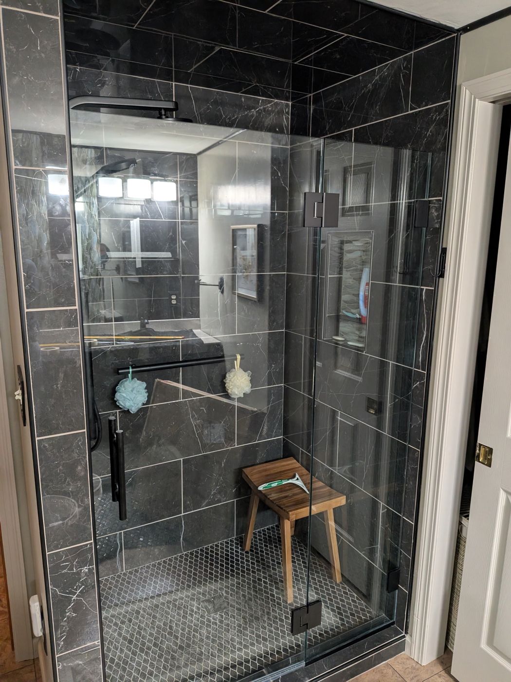 Frameless hinged shower enclosure in black marble tile bathroom